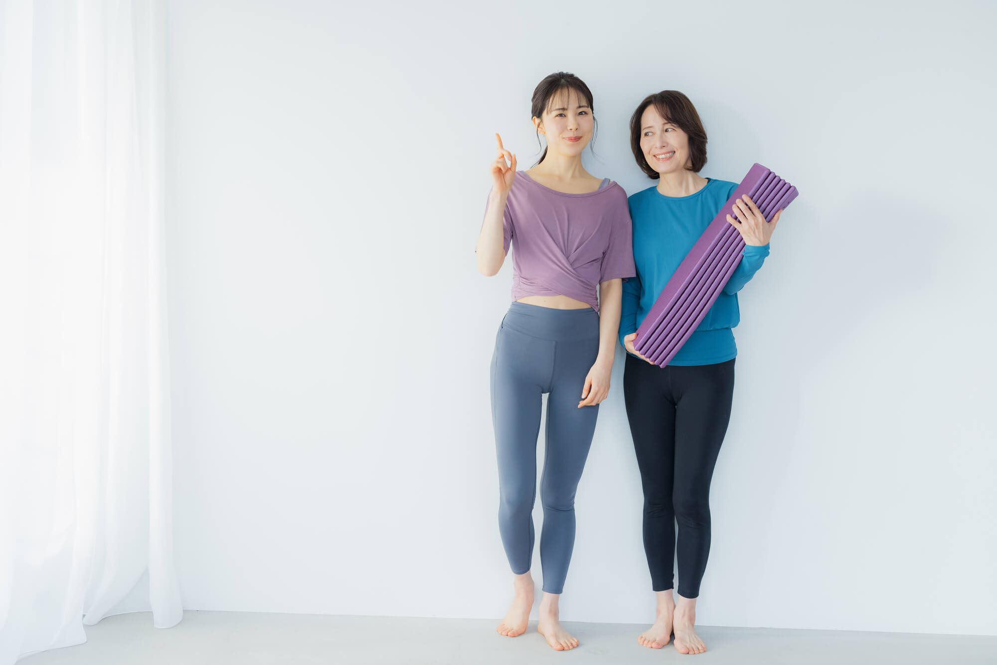 ヨガマットを持つ女性と人さし指を立てる女性