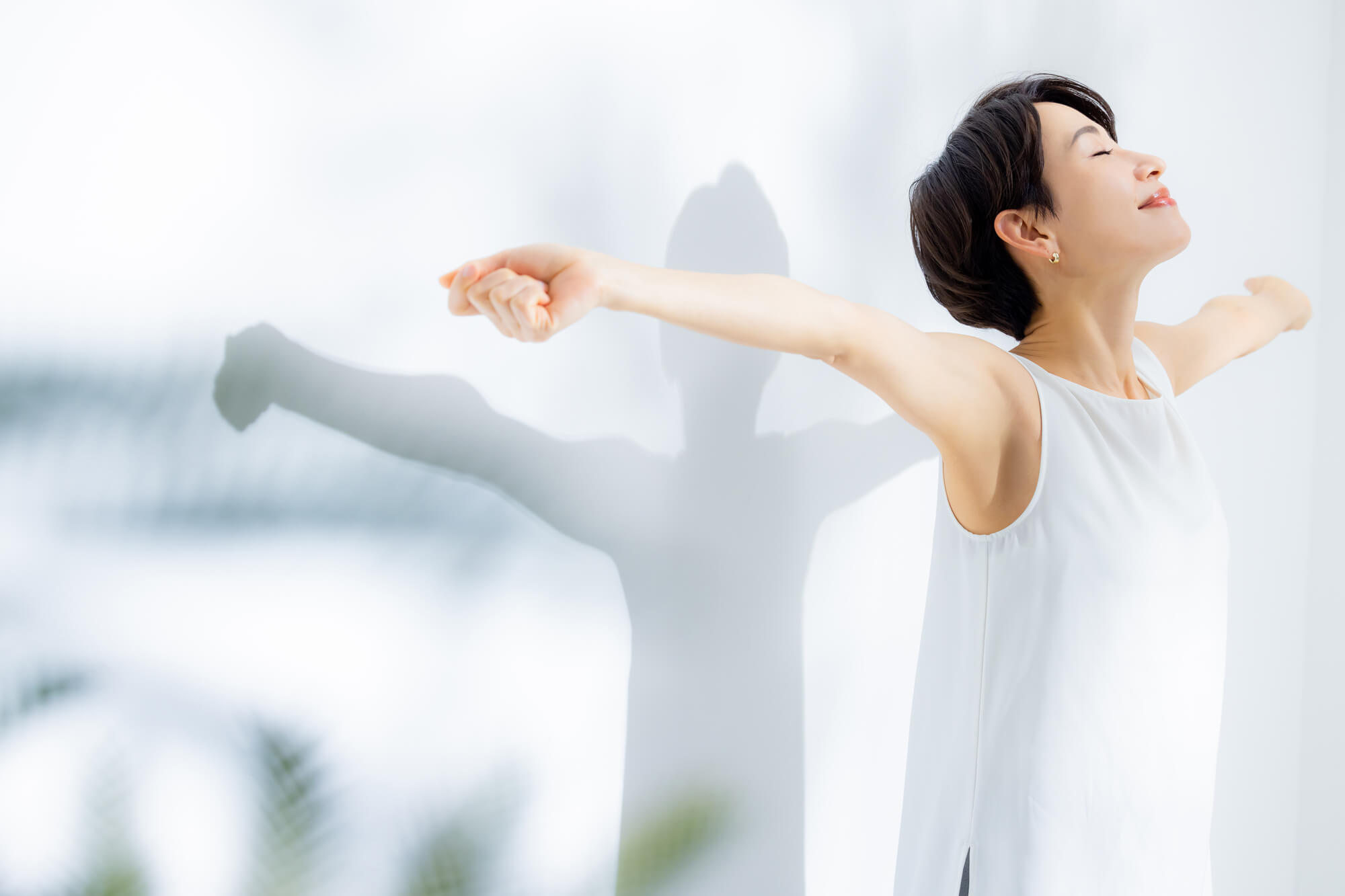 光に向かって気持ちよさそうに両腕を広げる女性