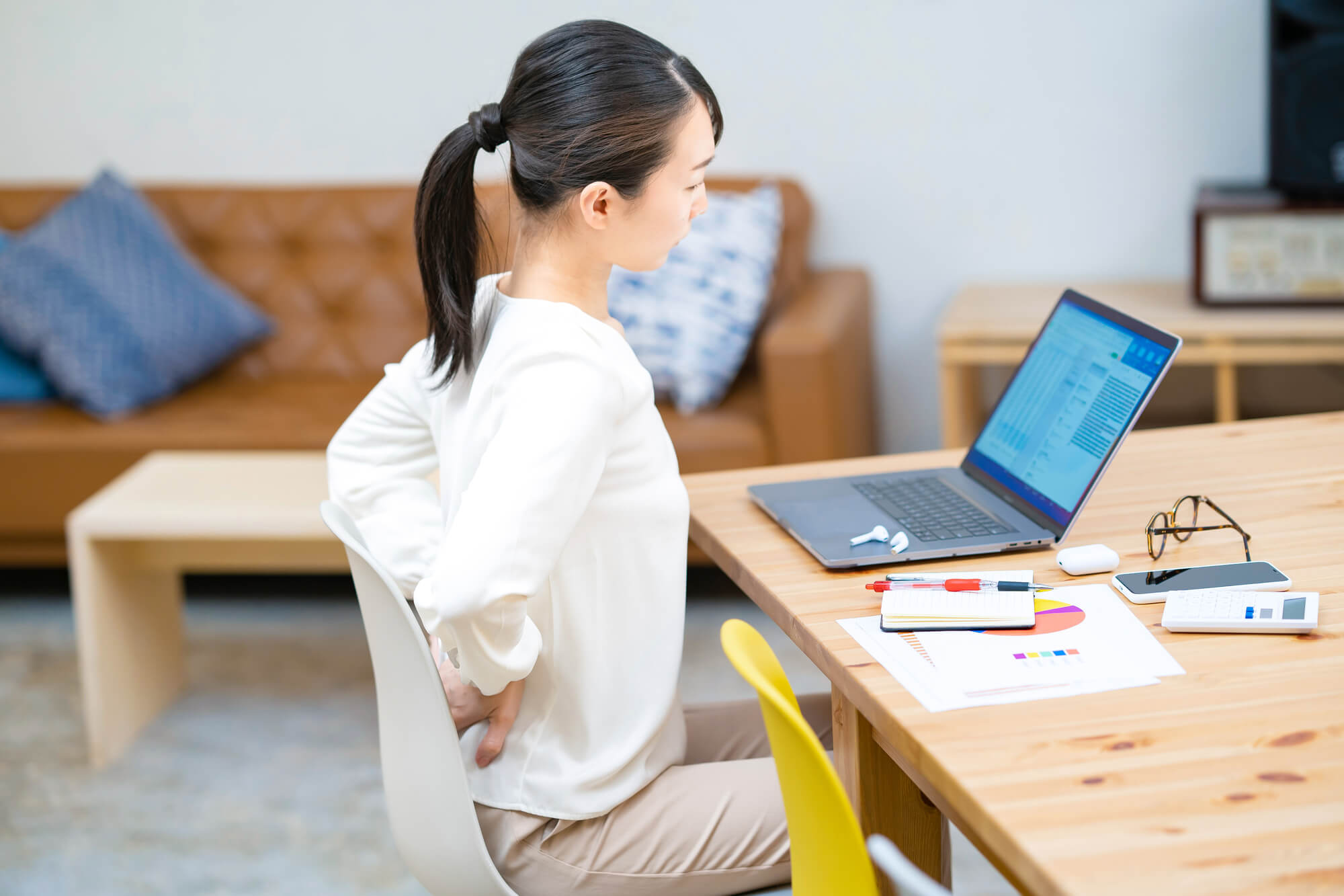 パソコン前で座りながら腰に手を当てる女性