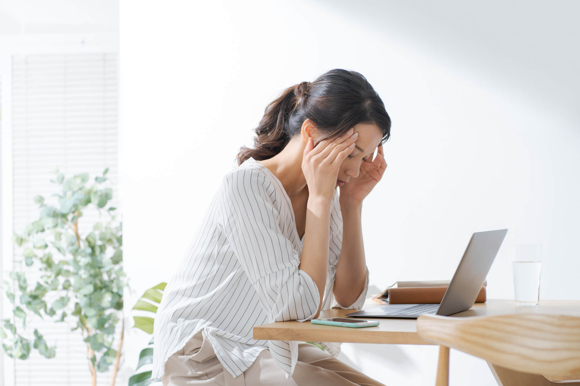 パソコンの前で、頭を押さえる女性