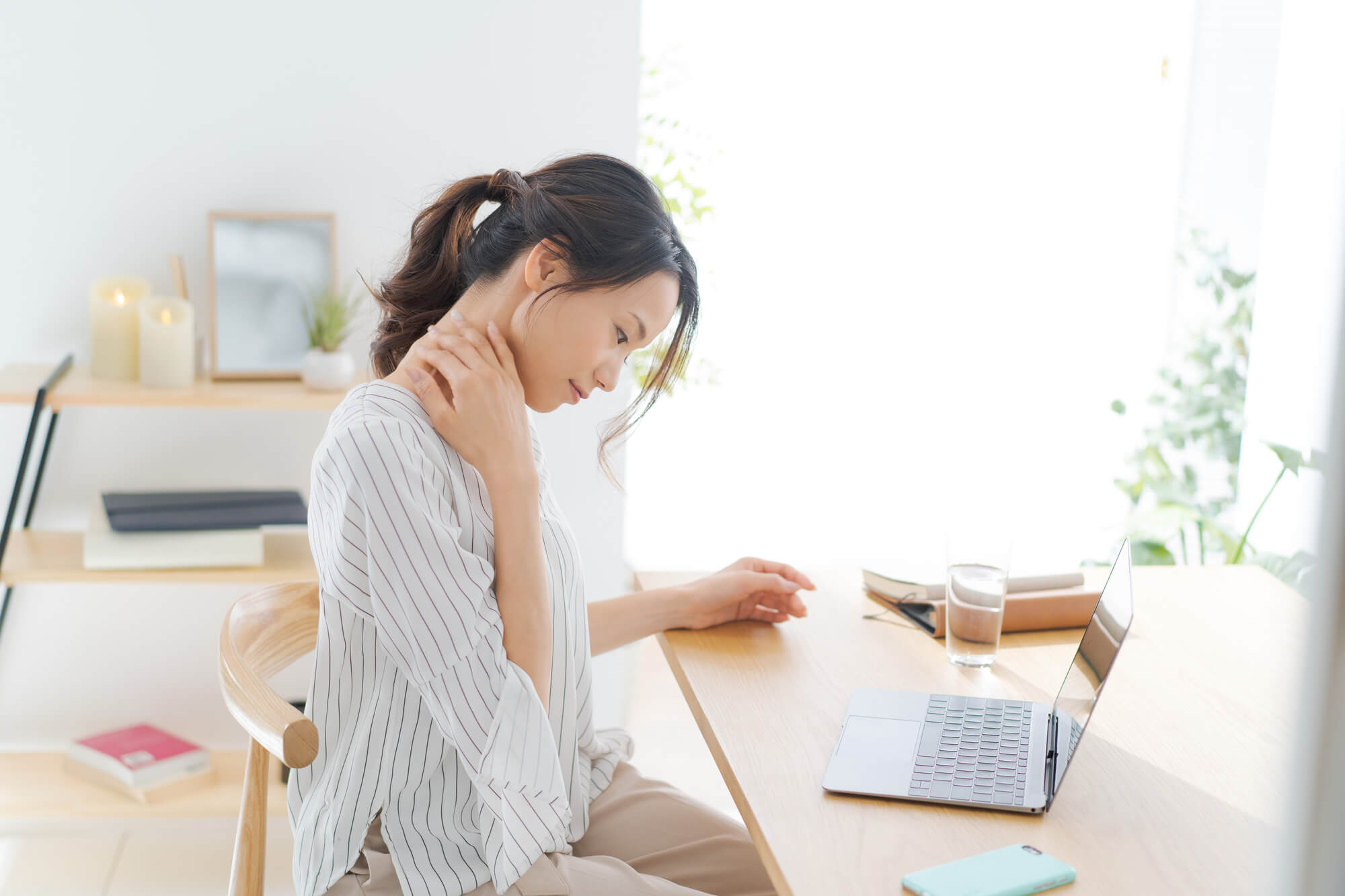 パソコンの置いてあるデスクの前で、首を触っている女性