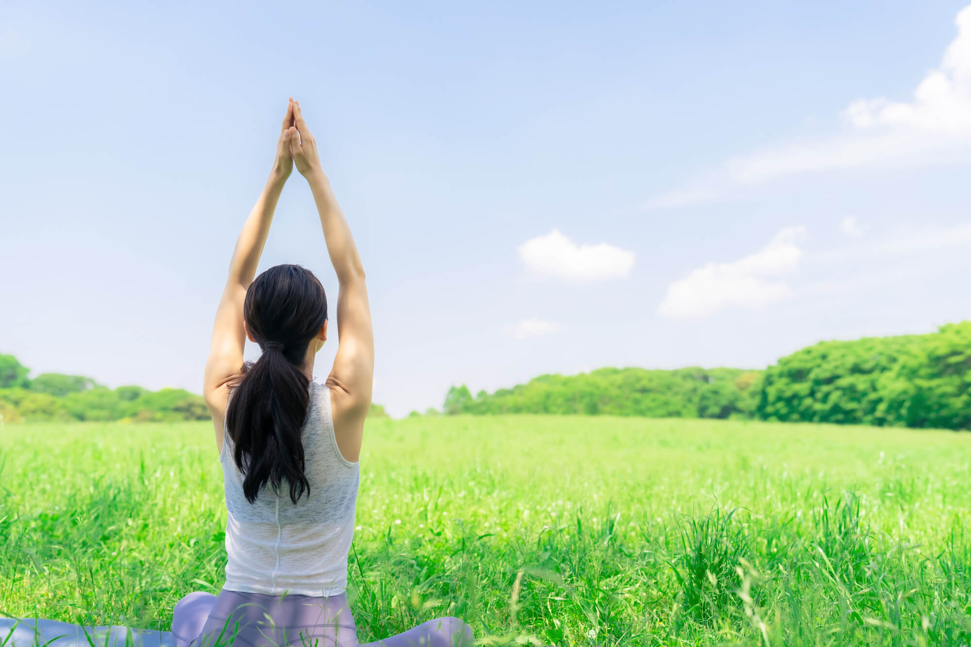 晴天の中、自然豊かな原っぱでピラティスをする女性の後ろ姿