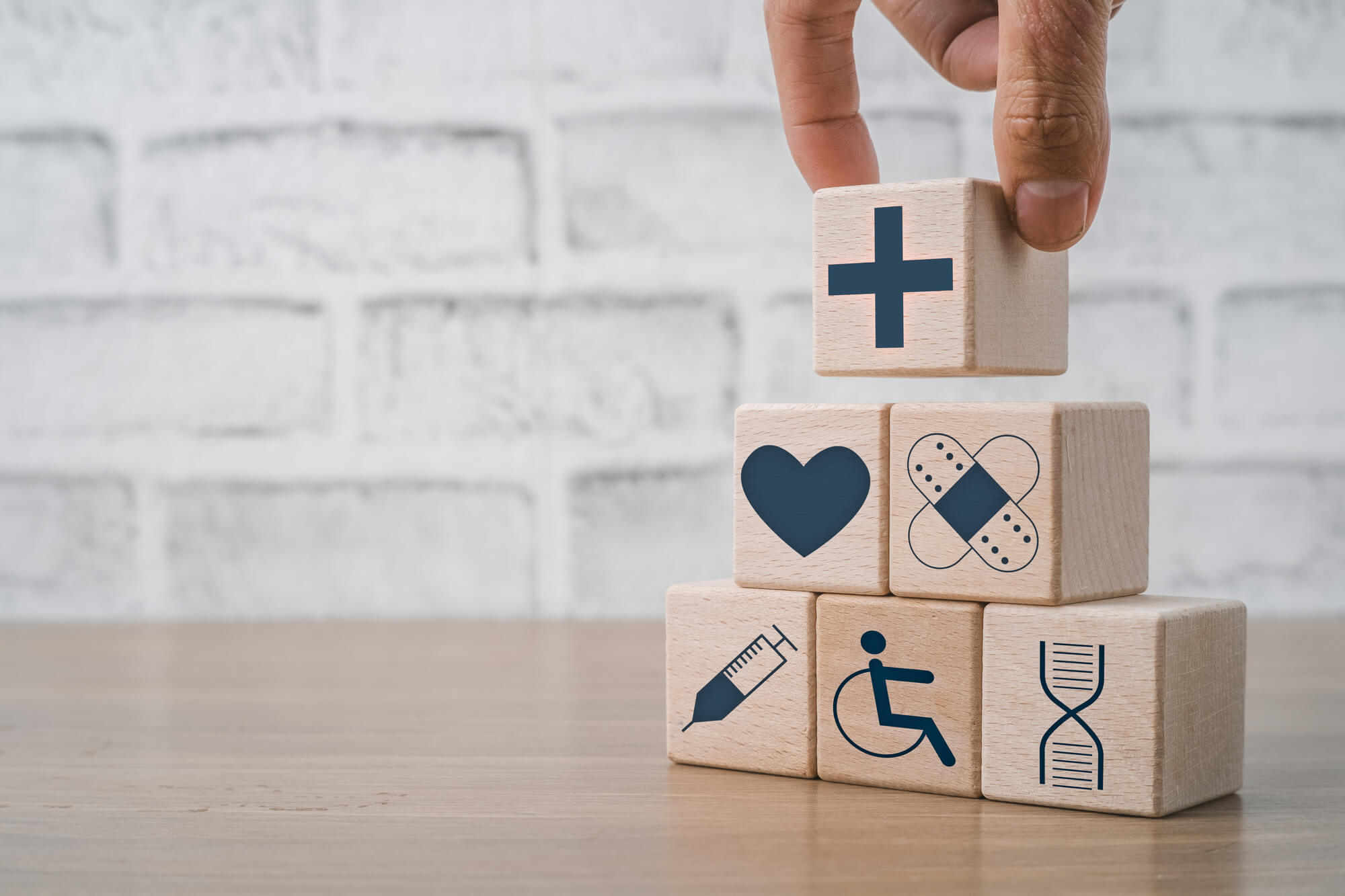健康・医療に関するイラストが描かれた積み木と、それを積み上げる人の手