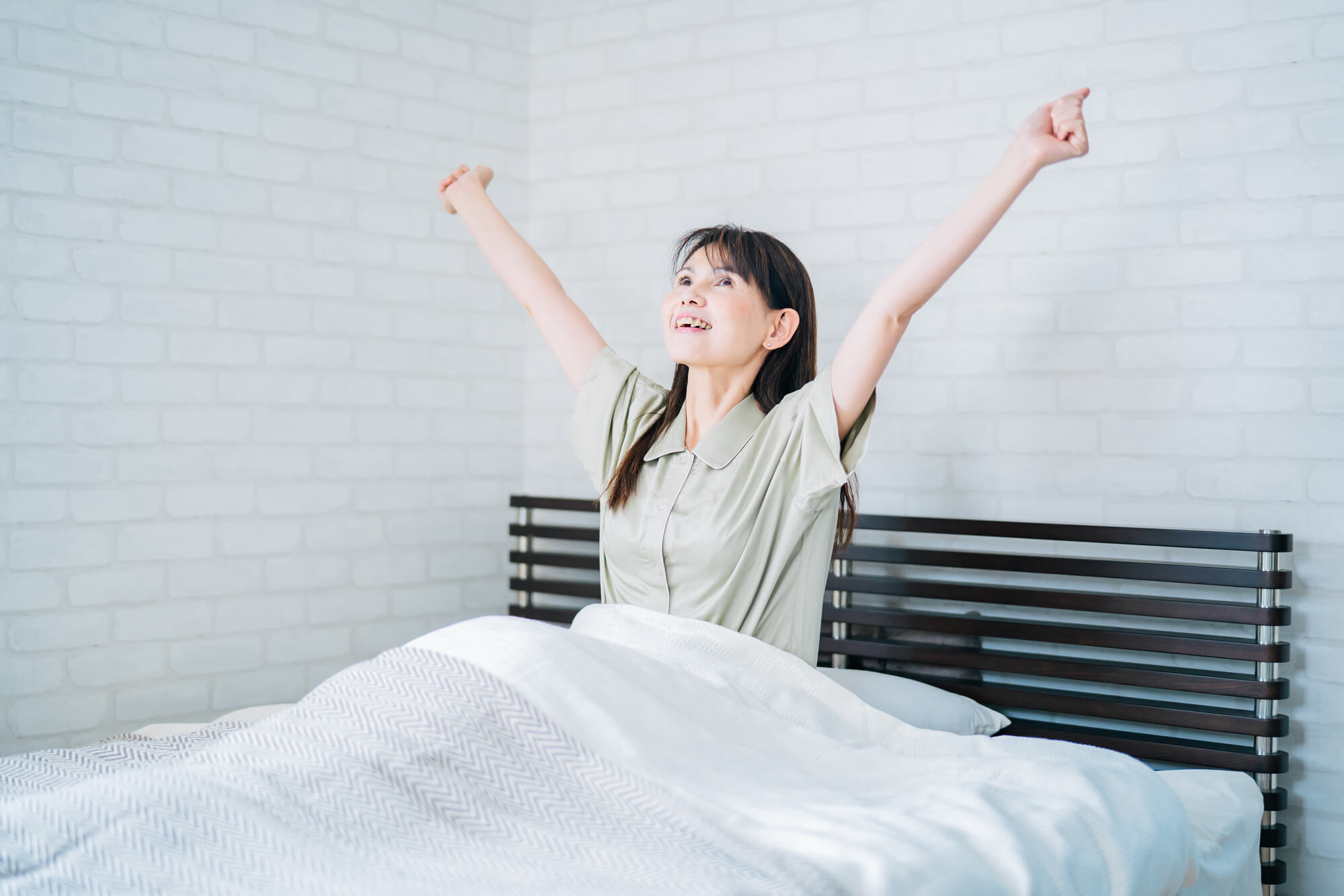 ベッドの上で両手を伸ばし大きく伸びをする女性