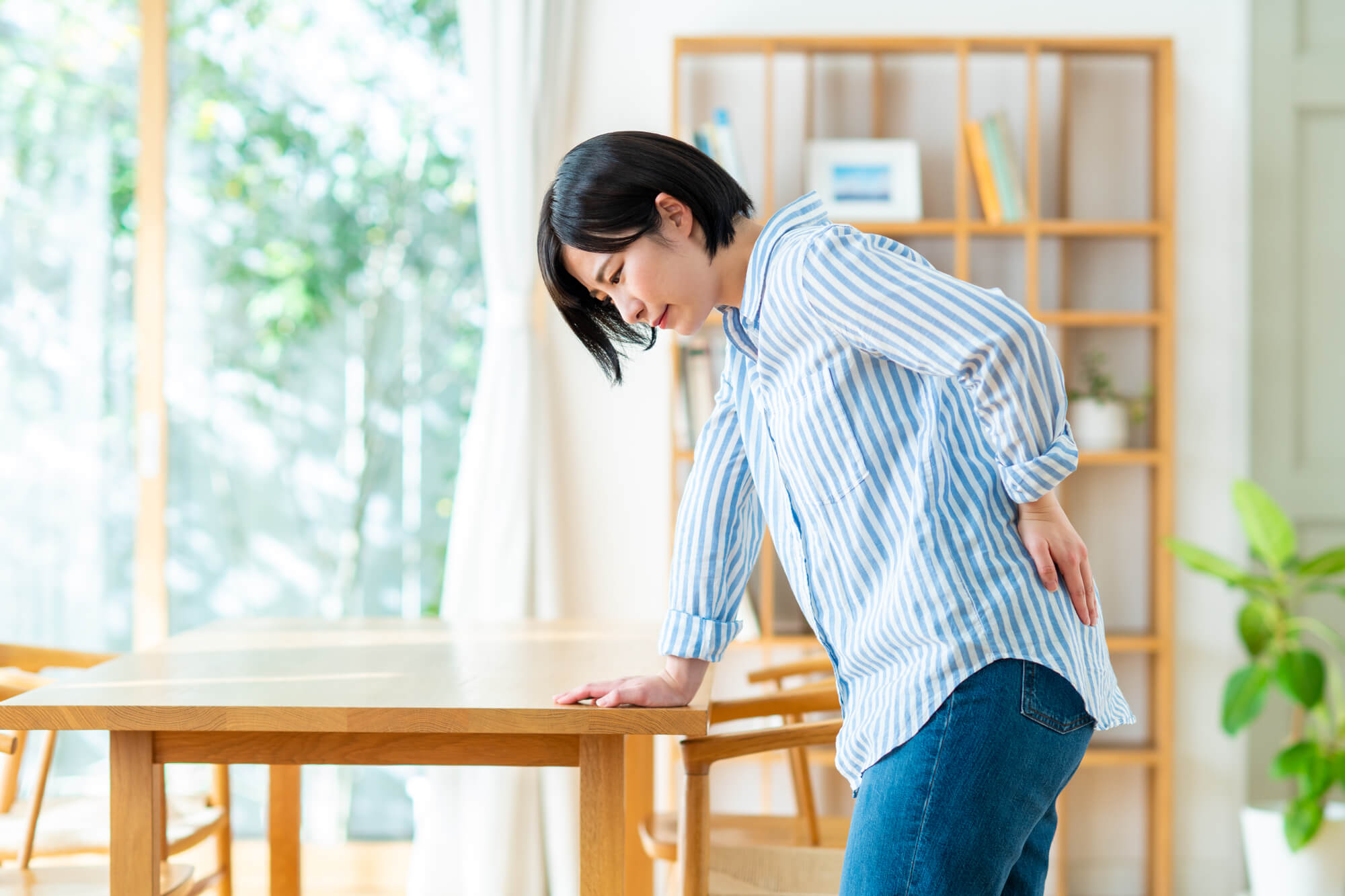テーブルに片手をつき、痛そうな顔で腰を触る女性