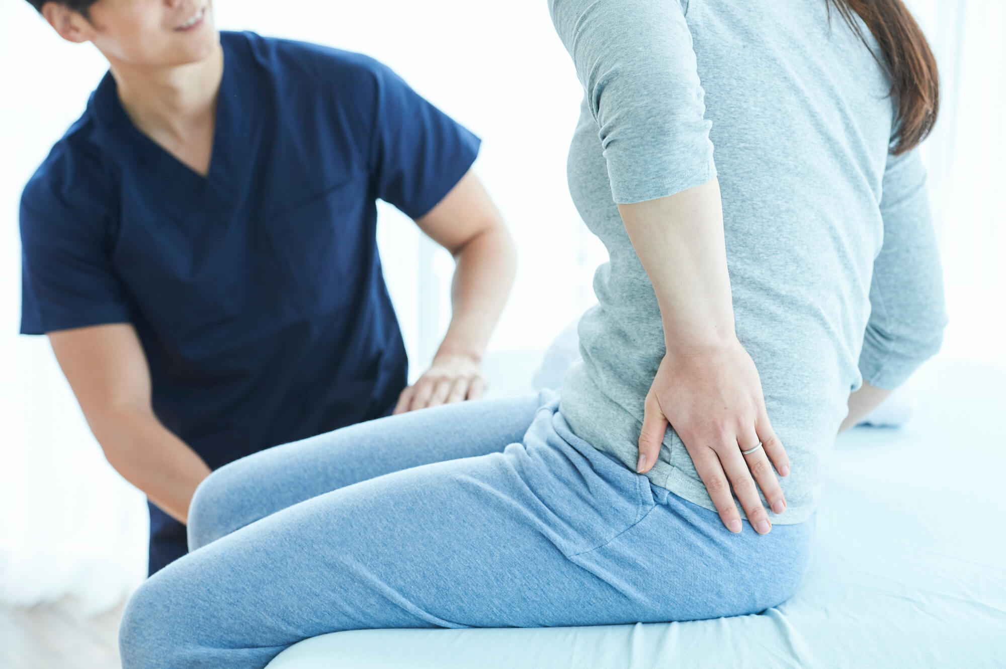 診察台に座り腰の辺りをおさえる女性と、様子をうかがう男性