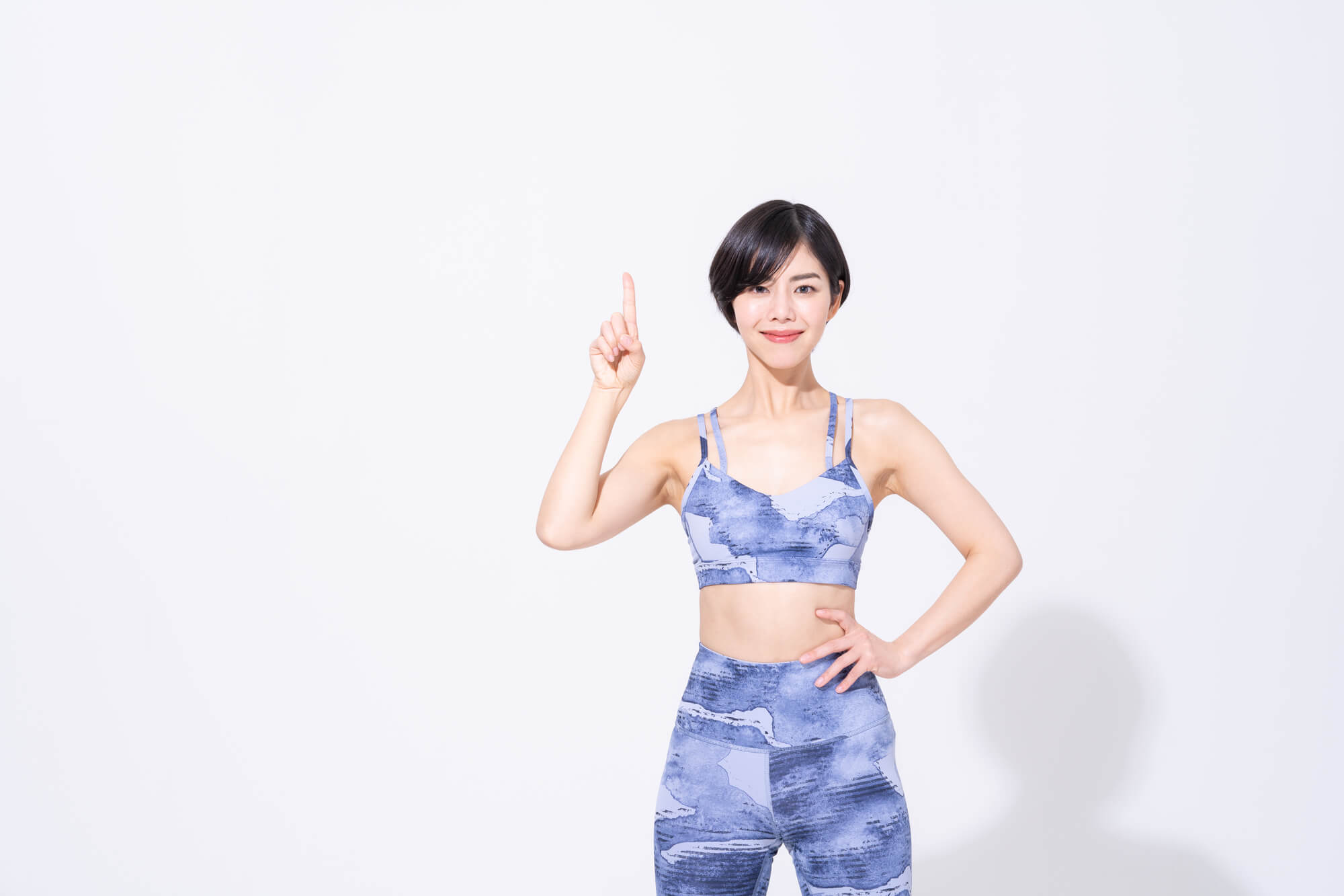 ヨガウェアを着用し、人さし指を上に向けて立っている女性