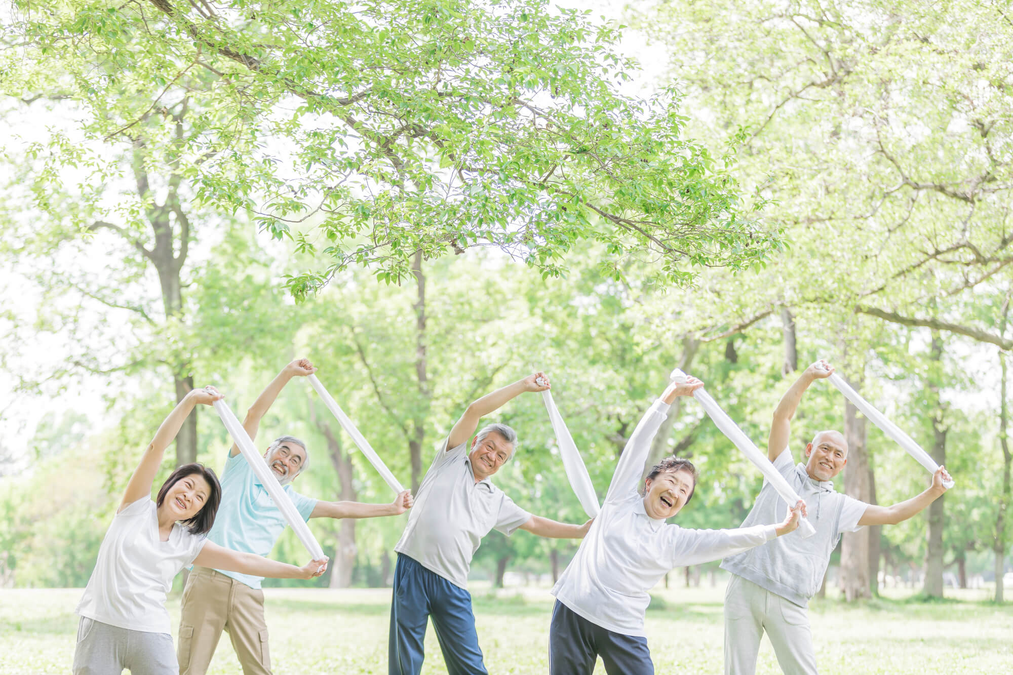 屋外でタオルを使った体操をしているシニアのグループ