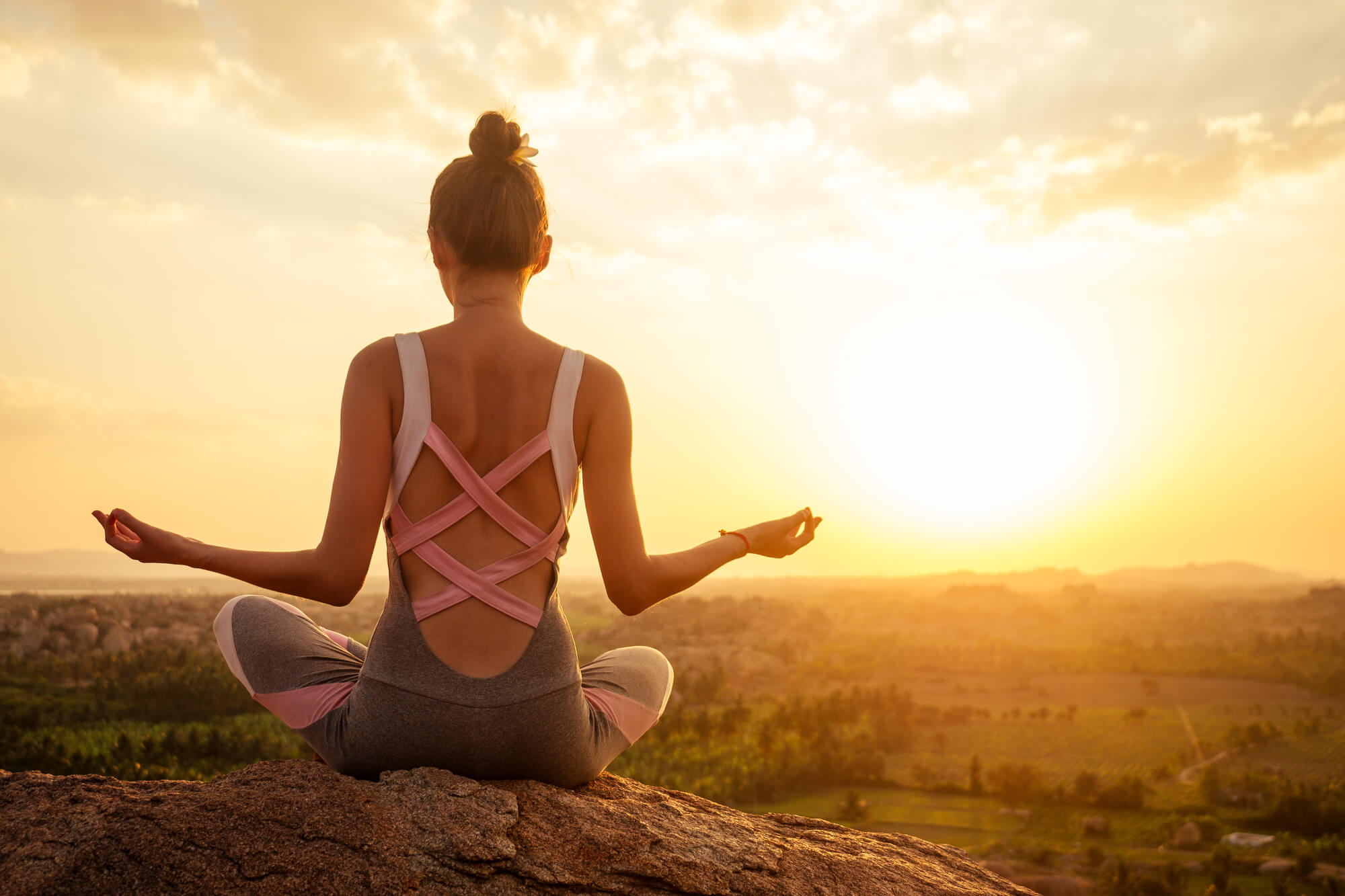丘の上で夕日を見ながらヨガをする女性
